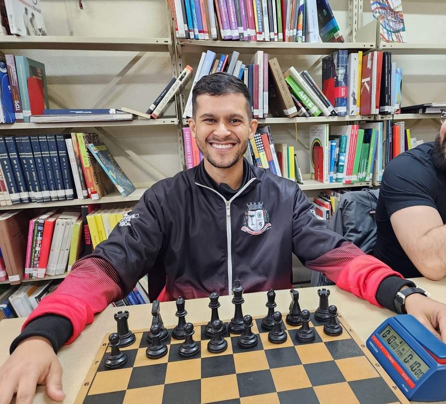 André, do Xadrez Taboão, sorrindo em frente a um tabuleiro de xadrez