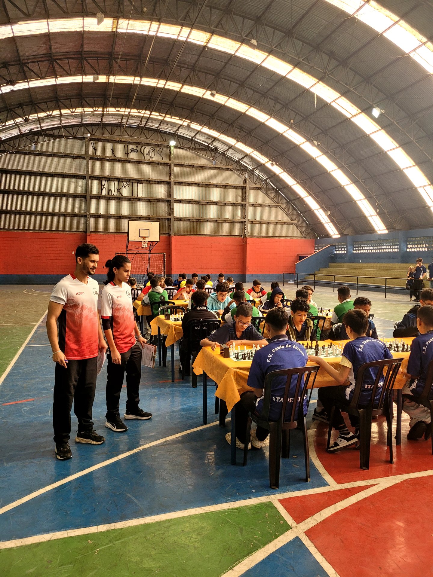 Simultânea de xadrez em quadra escolar com dezenas de alunos jogando
